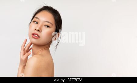Jeune femme asiatique avec maquillage naturel posant et regardant sur l'épaule, concept de beauté Banque D'Images
