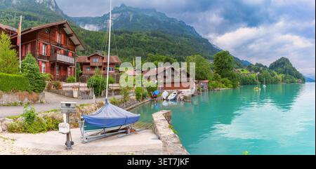 Village suisse traditionnel avec des maisons en bois et des bateaux amarrés sur la rive du lac de Brienz à Iseltwald, Suisse. Banque D'Images