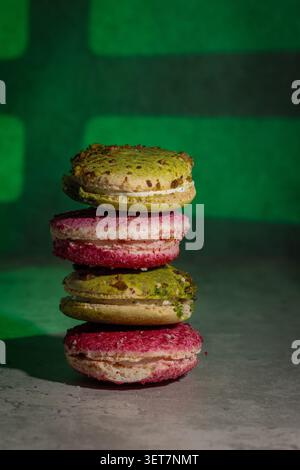 Macarons empilés dans des teintes roses et vertes éclatantes. Un éclairage doux projette de douces ombres autour des confiseries. Empiler légèrement incliné et lumière verte dans le Banque D'Images