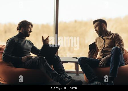 Deux hommes engagés dans la conversation avec les ordinateurs portables et le téléphone dans le bureau moderne, concept d'affaires Banque D'Images