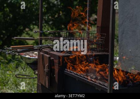 Barbecue au charbon de bois avec flammes nues et grilles de cuisson pendant la préparation pour la cuisson en plein air. L'image illustre la cuisson dans la cour arrière, la gestion des incendies Banque D'Images