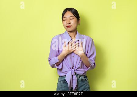 Jeune femme asiatique exprimant sa gratitude avec les mains sur le cœur, Joyful Emotion, Studio Setting Banque D'Images