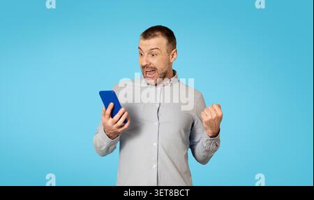 Homme caucasien excité célébrant la réalisation tout en utilisant smartphone, Business concept Banque D'Images
