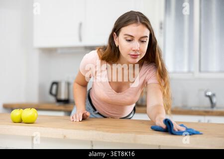 Femme nettoyant la table à manger avec un chiffon dans la cuisine à la maison Banque D'Images