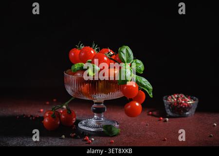 Tomates cerises au basilic dans un élégant bol à dessert sur une table sombre Banque D'Images