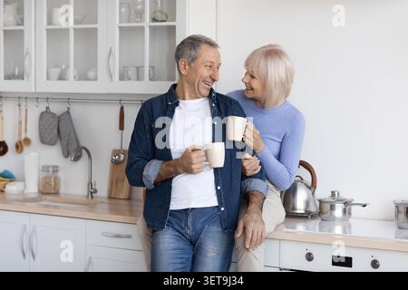 Heureux vieux couple caucasien appréciant le café ensemble dans Cozy Kitchen, souriant Banque D'Images