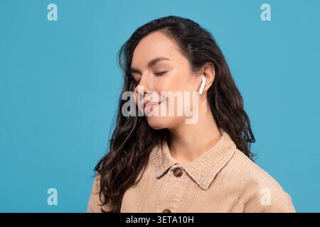 Jeune femme avec des écouteurs souriants et relaxants, fond bleu Banque D'Images