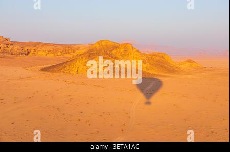 Vue aérienne de l'ombre d'une montgolfière jetée sur le sol du désert près de formations rocheuses de grès pendant l'heure dorée à Wadi Rum, Aqaba Governora Banque D'Images