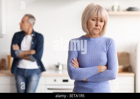 Inquiète femme caucasienne âgée regardant vers le bas avec expression déçue dans la cuisine Banque D'Images