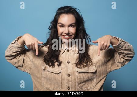 Sourire jeune femme hispanique pointant vers le bas avec les doigts, fond de studio, concept de style de vie Banque D'Images