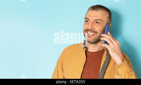Homme souriant parlant sur smartphone avec fond bleu, concept d'affaires Banque D'Images