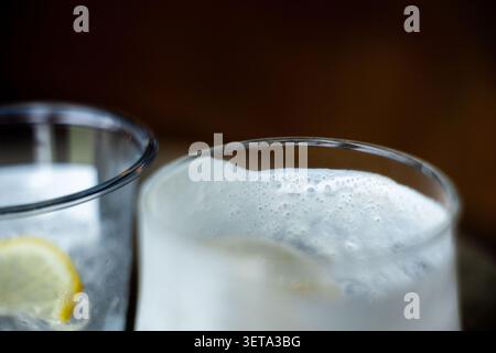 Gros plan de deux verres clairs avec de la glace, un avec une tranche de citron, boisson fraîche rafraîchissante, condensation sur le verre, boisson d'été, fond brun, relaxat Banque D'Images