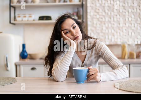 Triste jeune femme asiatique tenant la tasse de café à la maison, se sentant ennuyé et non motivé, concept de perte de poids Banque D'Images