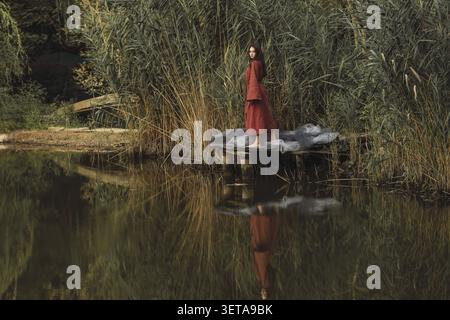 Authentique jeune femme dans une tunique en lin de style traditionnel debout sur un quai. Beau fond de nature avec feuillage d'été. Style de vie de haute qualité s Banque D'Images