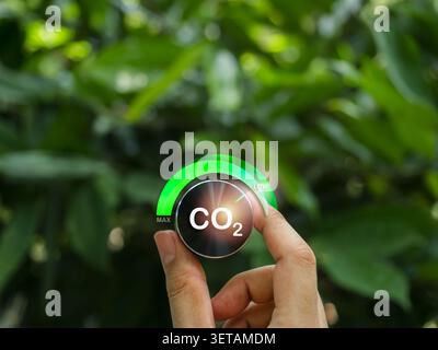 Main tournant le bouton de commande CO2 sur LOW pour environnement naturel vert. Réduction des émissions de carbone, contrôle du climat, objectifs nets zéro, durabilité et e Banque D'Images