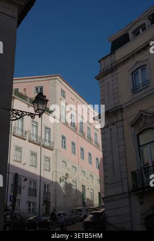 Gros plan de lampadaire en fonte noire ornée avec bâtiment rose pastel et ciel bleu profond à Lisbonne Banque D'Images