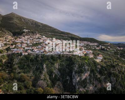 Une vue aérienne capture un charmant village grec construit dans une montagne verdoyante, avec de nombreuses maisons blanchies à la chaux avec des toits en terre cuite. Le Banque D'Images