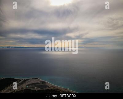 Une perspective aérienne capture le vaste océan bleu foncé rencontrant une côte marron clair et verte au premier plan. Les masses terrestres éloignées sont visibles o Banque D'Images