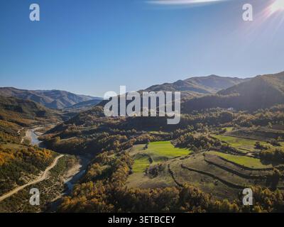 Une perspective aérienne capture une rivière et une route sinueuse traversant une vallée entourée de montagnes. Le paysage présente le feuillage d'automne, gre Banque D'Images