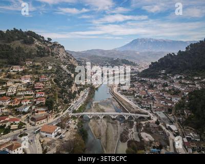Un plan large aérien capture la ville historique de Berat, en Albanie, avec la rivière Osum serpentant dans une vallée. Le pont Gorica relie les deux sid Banque D'Images