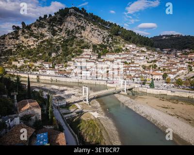 Une vue aérienne capture la ville historique de Berat, en Albanie, avec ses maisons blanches de l'époque ottomane regroupées sur une colline escarpée. La rivière Osum coule Thr Banque D'Images