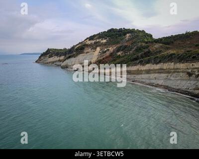 Une vue aérienne capture la mer Ionienne rencontrant une côte accidentée avec des falaises sédimentaires stratifiées surmontées d'une végétation dense verte et automnale Banque D'Images