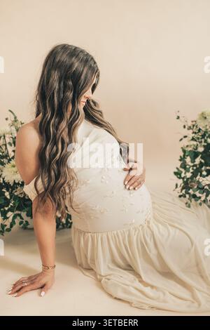 Femme enceinte en robe brodée assise tenant le ventre par des fleurs Banque D'Images