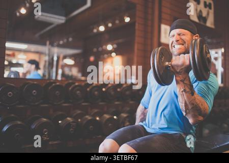 Homme tatoué musclé faisant des boucles de biceps au gymnase Banque D'Images