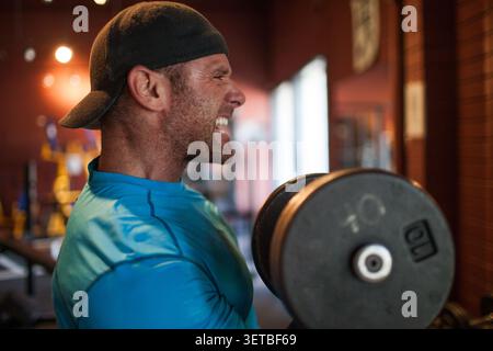 Homme tatoué musclé faisant des boucles de biceps au gymnase Banque D'Images