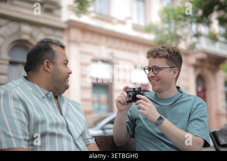 Un homme souriant prend une photo de son ami sur un banc de ville Banque D'Images