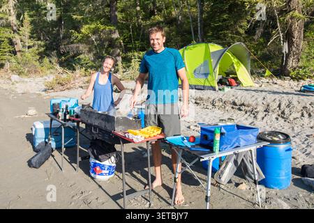 Heureux couple cuisinant le petit déjeuner à leur camping de plage Banque D'Images