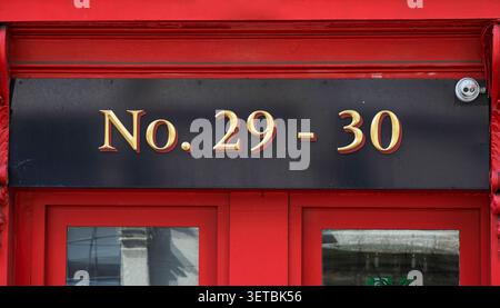 Détail de la façade de magasin irlandais vintage avec encadrement en bois peint cramoisi et lettrage d'adresse doré sur une rue de la ville montrant les numéros 29 et 30 Banque D'Images