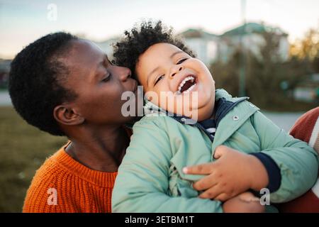 Mère aimante embrassant un enfant heureux à l'extérieur en ville Banque D'Images