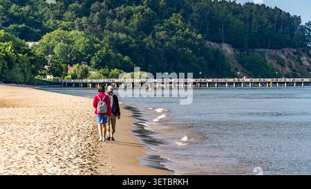 Couple senior marchant le long de la plage de la mer Baltique avec des sacs à dos le jour ensoleillé Banque D'Images