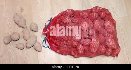 Vue aérienne d'un grand sac à mailles rouges rempli de pommes de terre à côté d'un tas de pommes de terre sales non lavées sur un plancher en bois Banque D'Images