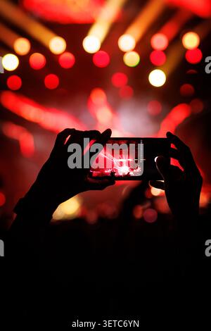 Vue rapprochée d'une personne tenant un smartphone horizontalement pour enregistrer une performance spectaculaire de concert en direct. L'écran affiche le cerf éclairé Banque D'Images