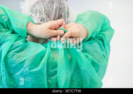 Le travailleur de la santé sécurise une blouse d’hôpital stérile avant d’effectuer une intervention, soulignant l’importance vitale du contrôle des infections et de la sanitat Banque D'Images