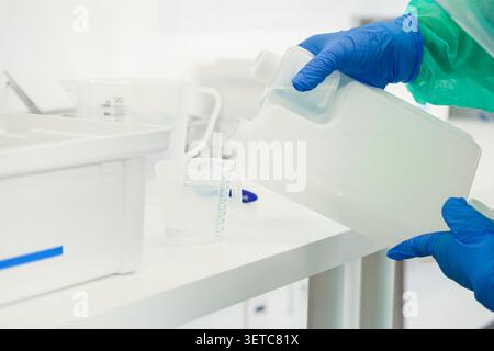 Un chercheur scientifique portant un équipement de protection et des gants effectue une procédure de mesure précise dans un laboratoire lumineux, mettant en évidence les protocoles de sécurité et Banque D'Images