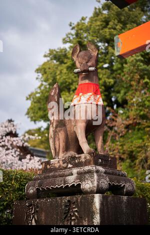 Statue de renard de kitsune en pierre avec bavoir rouge et parchemin dans un sanctuaire shinto à Kyoto Banque D'Images