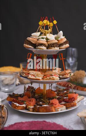 Présentoir à plusieurs étages avec hors-d'œuvre pour un événement festif. Les hors-d'œuvre délicieux comprennent des mini sliders, des sandwichs et des bruschettas. Variété de collations gastronomiques Banque D'Images