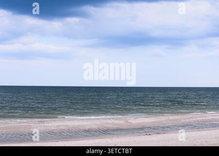 Le large horizon océanique rencontre le ciel nuageux au-dessus du rivage de la plage de sable. L'eau bleu profond de l'océan ondule sous de lourds nuages créant un paysage naturel spectaculaire. Min Banque D'Images