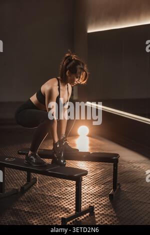 Jeune femme confiante travaillant avec kettlebell sur le banc dans un environnement de gymnastique élégant. Passionné de fitness dévoué faisant preuve de force, d'équilibre et de détermination dans une routine de style de vie actif Banque D'Images
