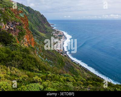 Une photo en grand angle capturant le village côtier de Paul do Mar niché entre d'imposantes falaises verdoyantes et l'océan, Madère, Portugal. Banque D'Images