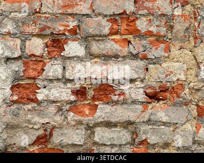 Gros plan d'un vieux mur de briques altérées avec du plâtre fissuré et des briques rouges exposées. Fond rustique de texture de maçonnerie grunge. Banque D'Images