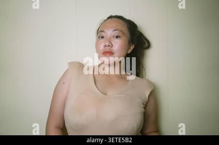 Jeune femme posant en toute confiance à l'intérieur contre un mur Uni, mettant en valeur la beauté naturelle, le style de vie décontracté, la confiance en soi. Banque D'Images