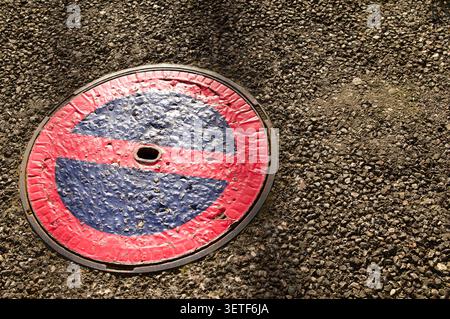 Vue de haut en bas d'un panneau de signalisation circulaire No parking peint sur un couvercle de trou d'homme en métal texturé dans la route asphaltée, avec un espace de copie sur la droite. A con Banque D'Images