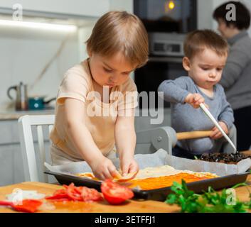 La famille cuisinent la pizza ensemble dans la cuisine à la maison confortable. Les enfants mignons avec une mère heureuse préparent la nourriture ou le repas pour le dîner Banque D'Images