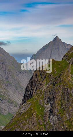 Vallée alpine spectaculaire dans les Lofoten avec d'imposantes falaises de basalte en colonnes, des pentes verdoyantes et une montagne à sommets distinctifs. Panoramique nordique Banque D'Images