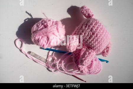 Boules de fil rose, crochet et morceaux de tissu faits à la main non finis sur une surface blanche brillante avec de fortes ombres de jour, montrant le travail artisanal créatif Banque D'Images