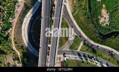 La vue aérienne capture l'échangeur routier complexe. Plusieurs ponts en béton relient les routes. Les véhicules se déplacent sur des voies courbes. La circulation est fluide Banque D'Images
